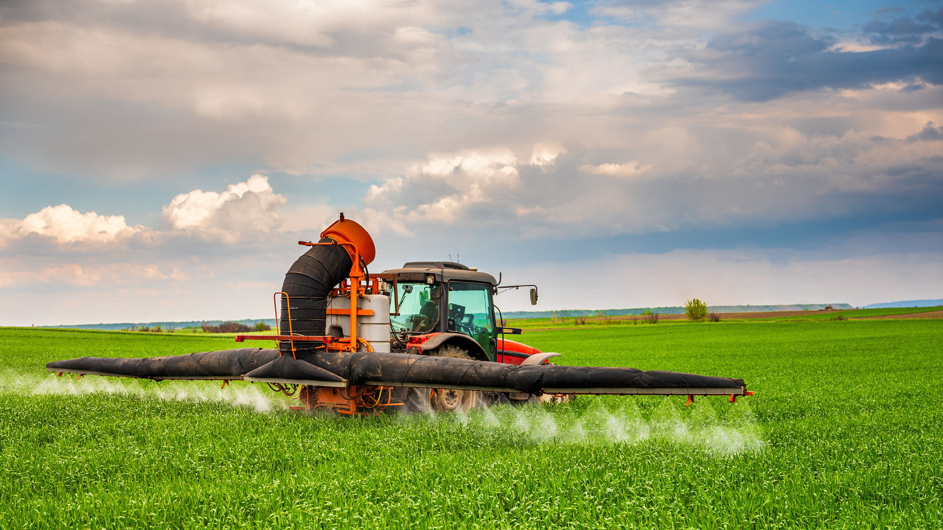Red tractor in green farm field applying SumaGroulx Microbial Product