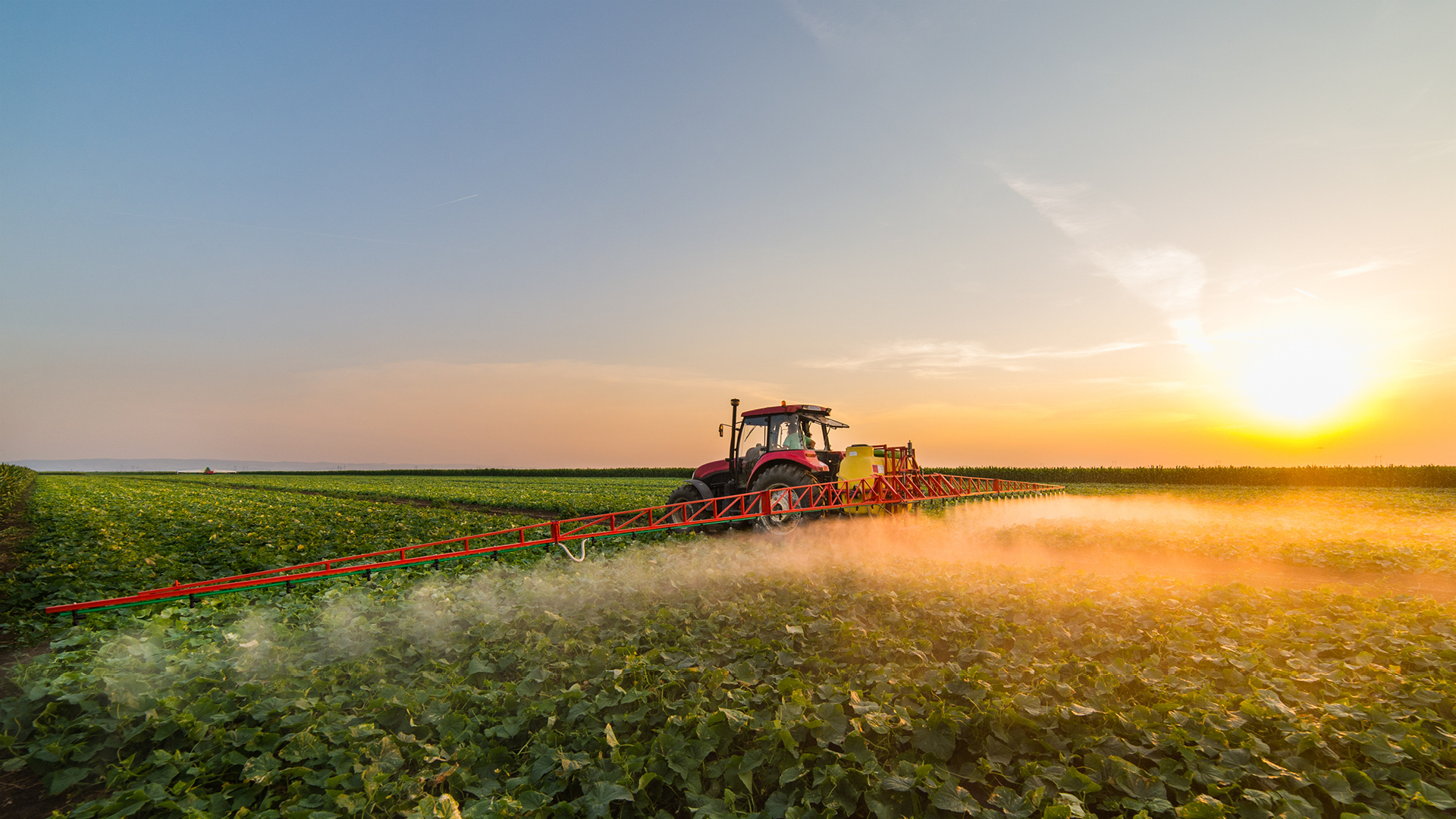 Red tractor in green farm field applying SumaGroulx Microbial Product with sunset in background